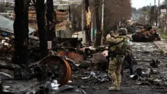 A serviceman uses his mobile phone to film a destroyed Russian tank in Bucha, in Kyiv region