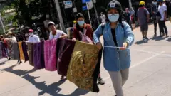 Women create a barrier across a street made of sarongs.
