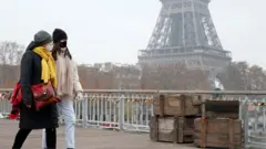 Women walk in front of the Eiffel Tower wearing Covid face masks, November 2021