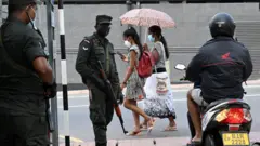 Pedestrians walk past soldiers standing on guard along a street in Colombo on 2 April 2022