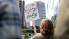 Mulher protestando do ladojogos para ganhar dinheiro de verdadefora do escritório da Amazon com uma placa que diz: 'Odeio me deslocar até o trabalho'.