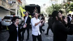 Israelenses dançam e cantam perto de um local residencial afetado, após um ataque de mísseis do Irã na cidade de Haifa