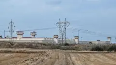 Silivri Cezaevi'nin duvarlarının önünde yüksek gerilim hatları ve bir tarla görülüyor