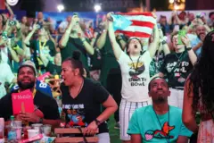 Fanáticos viendo el show de medio tiempo de Bad Bunny en el Super Bowl. Una mujer sostiene la bandera de Puerto Rico