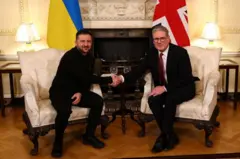 Presidente Zelensky da Ucrânia e o primeiro-ministro britânico Keir Starmer sentados, cumprimentando-se