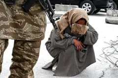 د ۲۰۲۶ کال د مارچ پر ۲۶مه، د کابل په عیدګاه جومات کې دویمې ډله ییزې جنازې د مراسمو پر مهال، یو طالب امنیتي ساتونکی ولاړ دی او یوه افغانه مېرمن، سمېره محمدي، د خپل زوی عارف خان په ویر کې ژاړي. عارف خان د پاکستان په هغه هوايي برید کې وژل شوی چې د روږدو کسانو د درملنې پر یو مرکز شوی و.