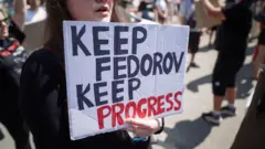 Una joven sostiene un cartel que dice: "MANTENGAMOS A FEDOROV, MANTENGAMOS EL PROGRESO".