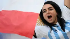 Tribünlerde Arjantinli bir kadın taraftar tezahürat yapıyor.