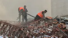 Members of di civil defence stand near one site wey don damage