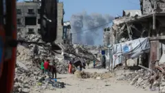 دخان يتصاعد في شمال قطاع غزة بينما يتنقل فلسطينيون مع عائلاتهم عبر جباليا هرباً باتجاه مدينة غزة