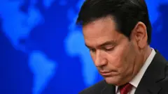 Rubio cabizbajo con un mapa detras en el que se ve el continente americano durante una conferencia de prensa en 2025