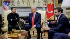 O presidente da Ucrânia, Volodymyr Zelensky (à esquerda), com as mãos cruzadas, reunido no Salão Oval com o presidente dos EUA, Donald Trump (centro), e seu vice-presidente, JD Vance (à direita). Os três estão sentados, e Trump e Vance gesticulam com a mão em sinal de desagrado em direção a Zelensky