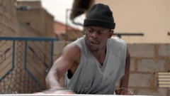 Foto de Arnold Ncube, tirada da cintura para cima. Ele está usando uma regata cinza com decote em V e um gorro preto. Seu braço direito está ligeiramente desfocado porque ele está limpando um carro