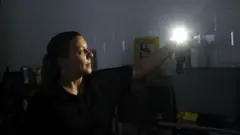 A woman uses her mobile phone torch inside a store during a power outage, in Madrid, Spain, 28 April 2025.