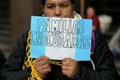 Mujer entre cadenas con un cartel que dice Familias Endeudadas