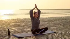 Kobieta ćwiczy jogę na oświetlonej słońcem plaży