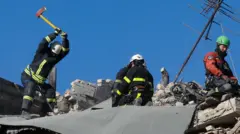 Фигуры четырех спасателей на крыше дома, поврежденного российским ударом. Первый замахивается топором, еще два сидят на коленях, четвертый - сидит на обломках конструкции крыши около телевизионной антенны