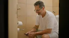 Homem sentado no vaso sanitário com seu telefone celular