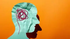 ورقة مقصوصة على شكل أكتاف ورأس إنسان بلون أخضر فاتح وبداخل الرأس خيوط حمراء في إشارة إلى دماغ مرتبك، على خلفية برتقالية. تعبر الصورة عن التنوع العصبي.