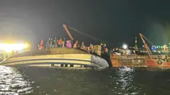 صورة تظهر قارباً منقلباً في خليج هالونج بمقاطعة كوانج نينه في فيتنام، بينما يقف غواصون من خدمات الطوارئ للتعامل معه.