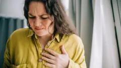 হৃদরোগ বোঝাতে প্রতীকী ছবি, একজন নারী বুকে একটি হাত দিয়ে ব্যাথ্যার ভঙ্গি করছেন