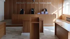 Boş bir mahkeme salonunda, mahkeme heyetinin yer aldığı kürsüde dosyaların yığıldığı görülüyor.
