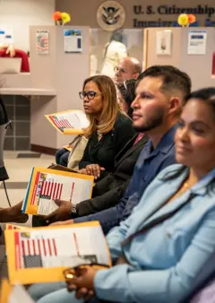 Varias personas sentadas en una sala con documentos de naturalización de EE.UU. en las manos