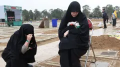 Two women crouch at the grave of a relative in a cemetary in Tehran on 16 March
