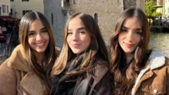Uma foto em que aparecem as três irmãs com casacos e sorrindo para a câmera.