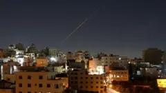 Um rastro de míssil corta o céu acima dos edifícios