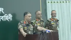 টেবিলে হাত রেখে কথা বলছেন মেজর জেনারেল মো.হাকিমুজ্জামান, তার পাশে আরও দুই জন সেনা কর্মকর্তা