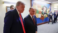 Трамп и Путин в коридоре на фоне карты штатов США, сзади видны люди с камерами.