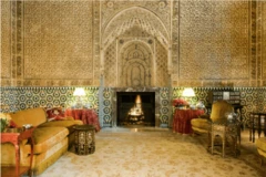 Fotografía interior de un palacio con ricos muebles amarillos y rojos, suelo de baldosas y paredes elaboradamente talladas.