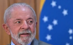 O presidente Lula e uma bandeira do Brasil logo atrás dele, desfocada