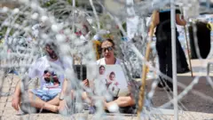 Lishay Lavi, mujer del rehén Omri Miran, secuestrado por Hamás, sentada entre alambradas junto a un hombre en una protesta en Tel Aviv.
