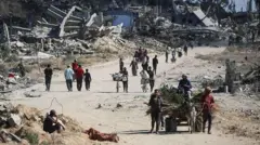 Palestinos desplazados caminan junto a edificios destruidos mientras regresan a sus hogares en la zona de al-Zahra, al norte del campo de refugiados de Nuseirat, en el centro de la Franja de Gaza, el 14 de octubre de 2025, un día después de que entrara en vigor un alto el fuego.