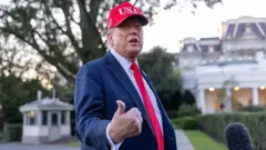 O presidente americano, Donald Trump, de terno e boné vermelho, fala nos jardins da Casa Branca