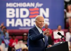 Ex-presidente americano Joe Biden de terno azul em discurso de campanha à reeleição, tendo ao fundo um cartaz de apoio do Estado de Michigan à sua candidatura