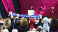 Erdoğan akp kadın kolları toplantısında kürsüde kadınlar ayakta arkaları dönük görünüyorlar. 
