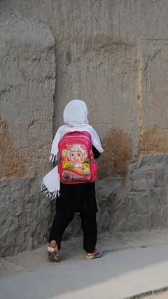 یوه افغانه نجلۍ چې د ښوونځي بکس یې په شا کړی دی او روانه ده