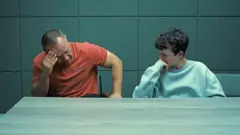 Pai e filho sentados preocupados em cena de Adolescência