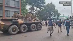 রাস্তা দিয়ে যাচ্ছে সেনাবাহিনীর ট্যাংক, ওপরে অস্ত্র হাতে বসে আছেন কয়েকজন সেনাসদস্য। পাশ দিয়ে হেঁটে যাচ্ছেন পুলিশ ও অন্যান্য আইনশৃ্ঙখলা বাহিনীর কয়েকজন সদস্য