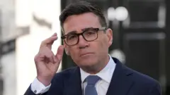 Umushikiranganji wa mbere mushasha w'Ubwongereza, Andy Burnham, yambaye amarori, ikositime yirabura n’ishati yera.