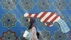 امرأة إيرانية تمر أمام جدارية لمسدس بألوان العلم الأمريكي على جدار السفارة الأمريكية السابقة في طهران، 28 مايو/أيار 2007. 