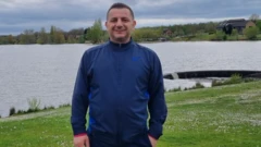 Orhan Ekren bir göl arka planında fotoğraf çektiriyor.