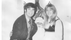 一張黑白照片中，卡羅爾先生與韋伯女士坐在聖誕老人的腿上，對著鏡頭微笑。