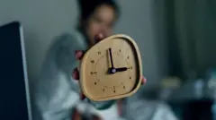 Pessoa sentada na cama mostra um despertador marcando três horas