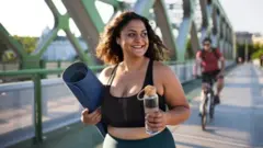 Moça parda de roupa de ginástica segurando uma água 