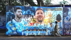 फ़ुटबॉल खिलाड़ियों के पोस्टर के आगे से गुज़रता व्यक्ति