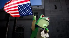 A frog costume protester holds a US flag upside down during a protest in LA